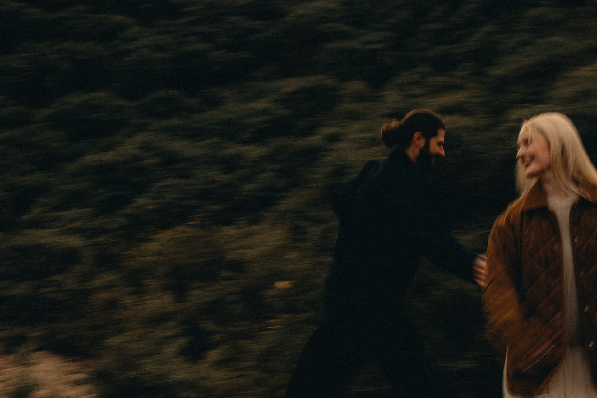 A couple laughing together mid-motion in a dark forest